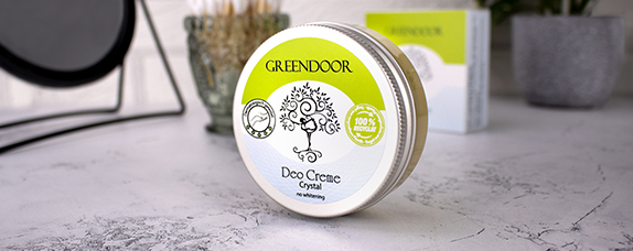 Eine Dose GREENDOOR Deo Creme Crystal mit 100% natürlichen Inhaltsstoffen auf einem Tisch, umgeben von weiteren Pflegeprodukten.